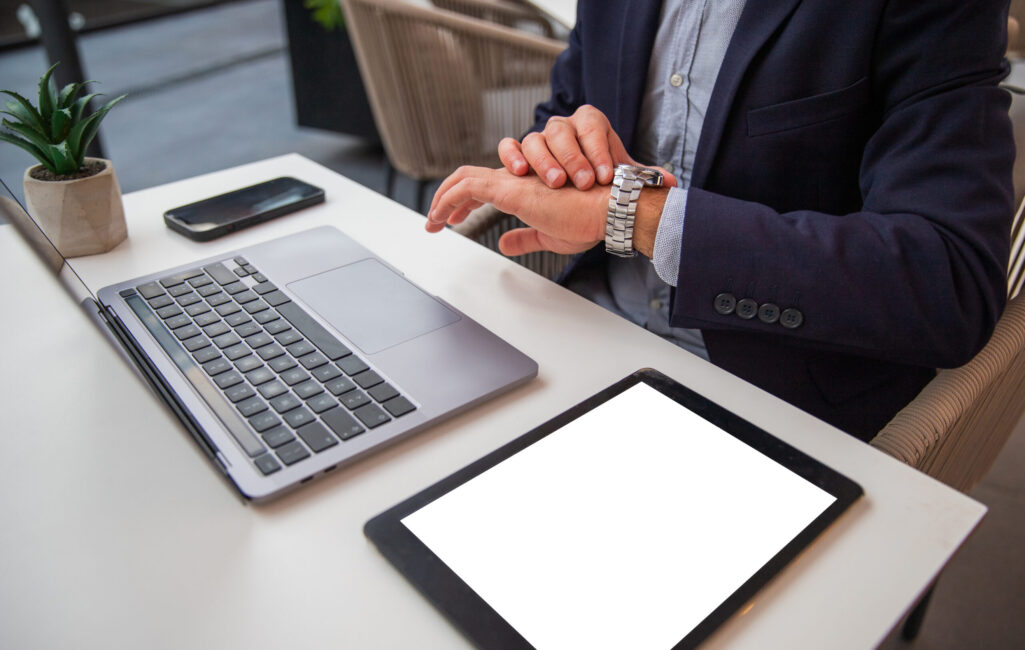Businessman's desk, he checks the time on his watch, blank tablet screen for mock up.